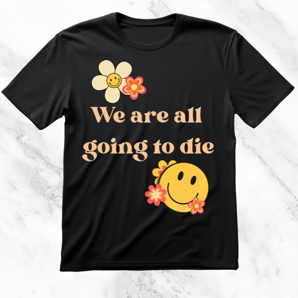 Black T-shirt featuring the phrase 'We Are All Going to Die' with playful floral illustrations and a smiling face, juxtaposing a dark existential statement with bright, cheerful imagery.